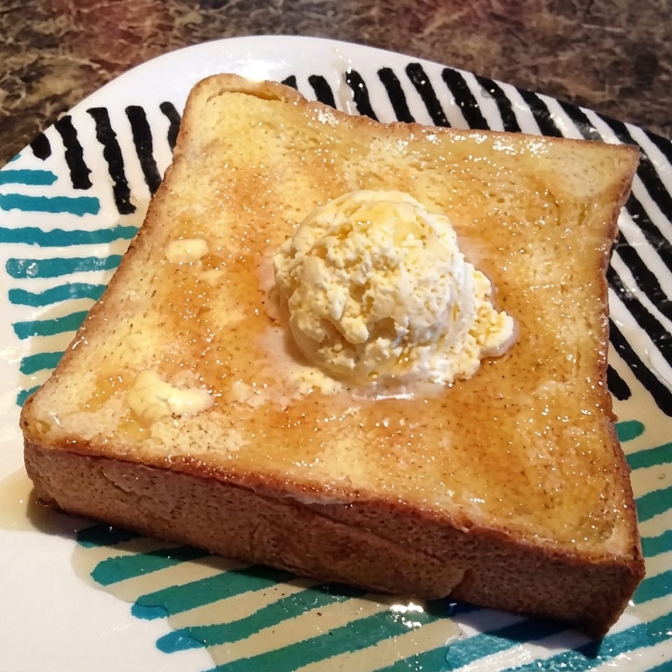 Golden French toast topped with melting butter, maple syrup, powdered sugar, and whipped cream on a colorful striped plate.