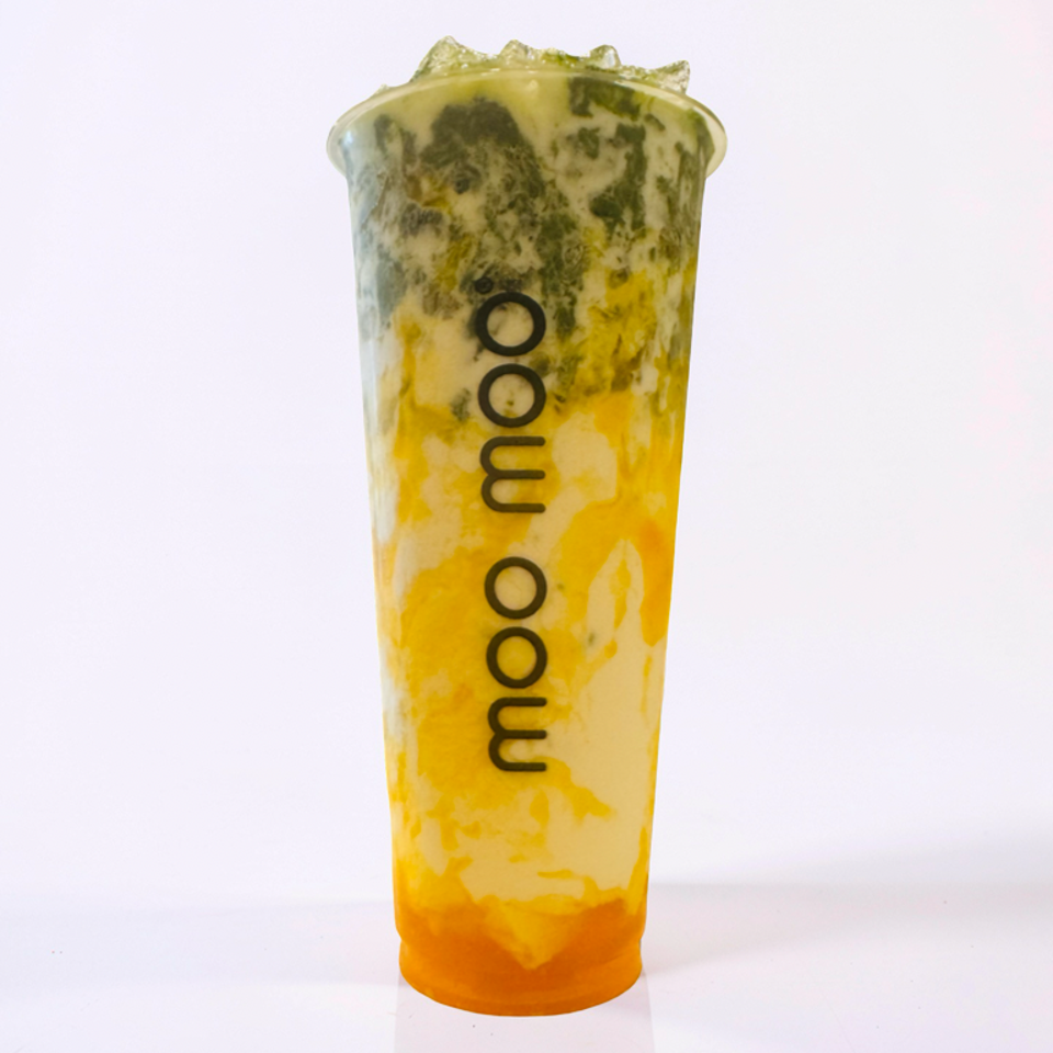 Tall MooMoo cup of yellow-orange mango matcha drink with green matcha swirls and ice, displayed against a white background.