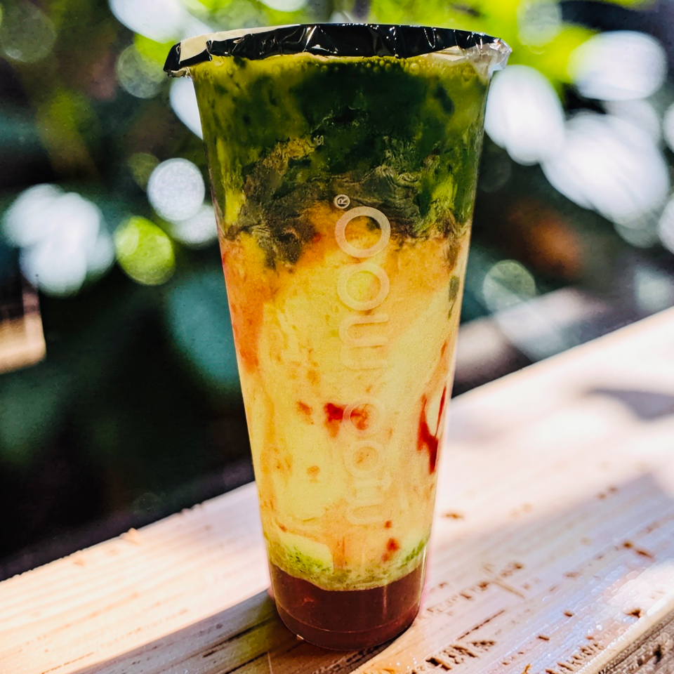 Layered matcha strawberry drink in a sealed cup on a rustic wooden table, with blurred berries in the background.